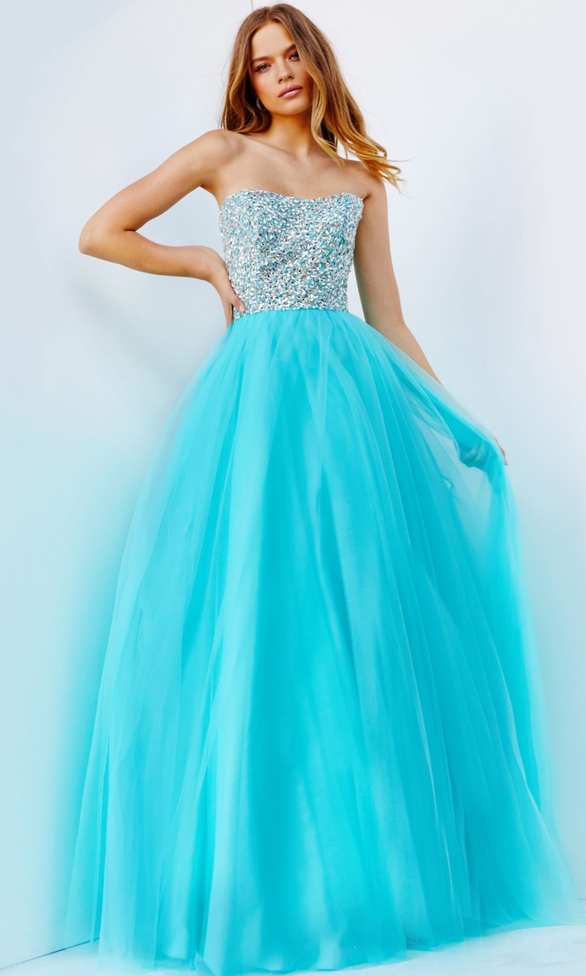 A woman stands against a light background wearing the Jovani 52131 Long Strapless Ball Gown Prom Dress featuring a beaded bodice and a full turquoise tulle skirt.